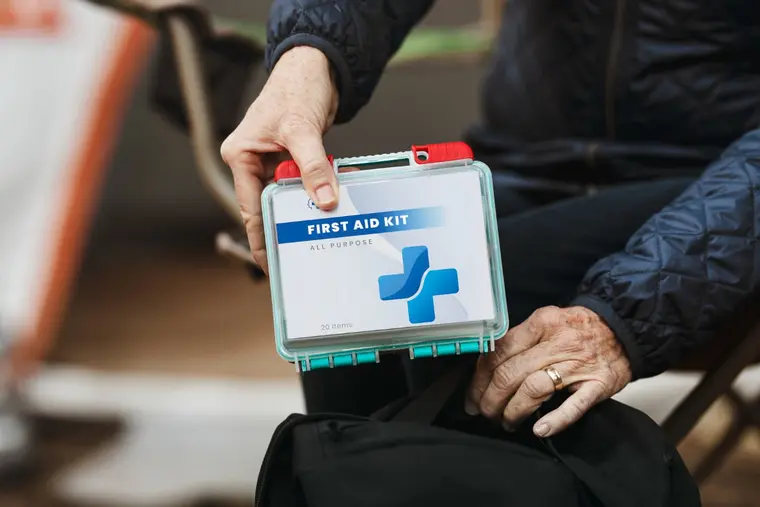 Two hands holding a clear all-purpose first aid kit box over an open black bag.